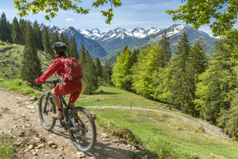 Un uomo con abito tecnico sportivo rosso percorre con una mountain bike un sentiero di montagna con panorama