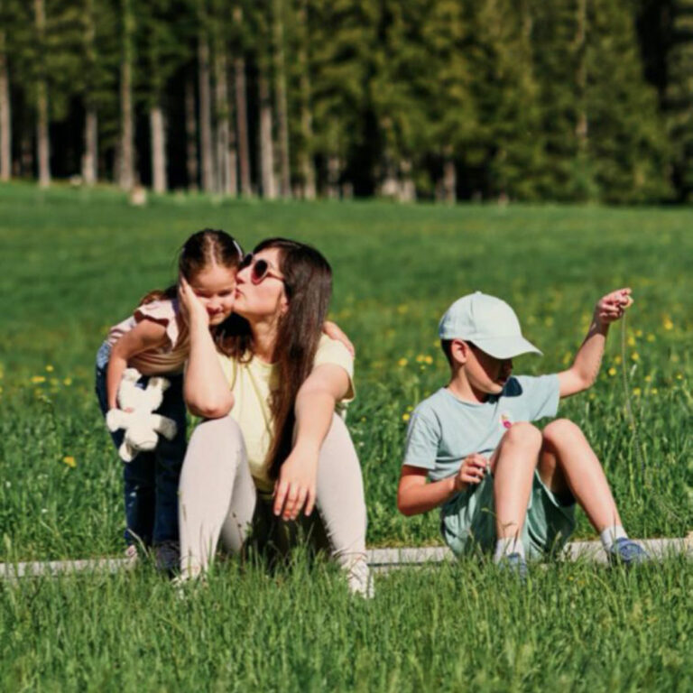 Una mamma con 2 bambini seduti sul prato in montagna