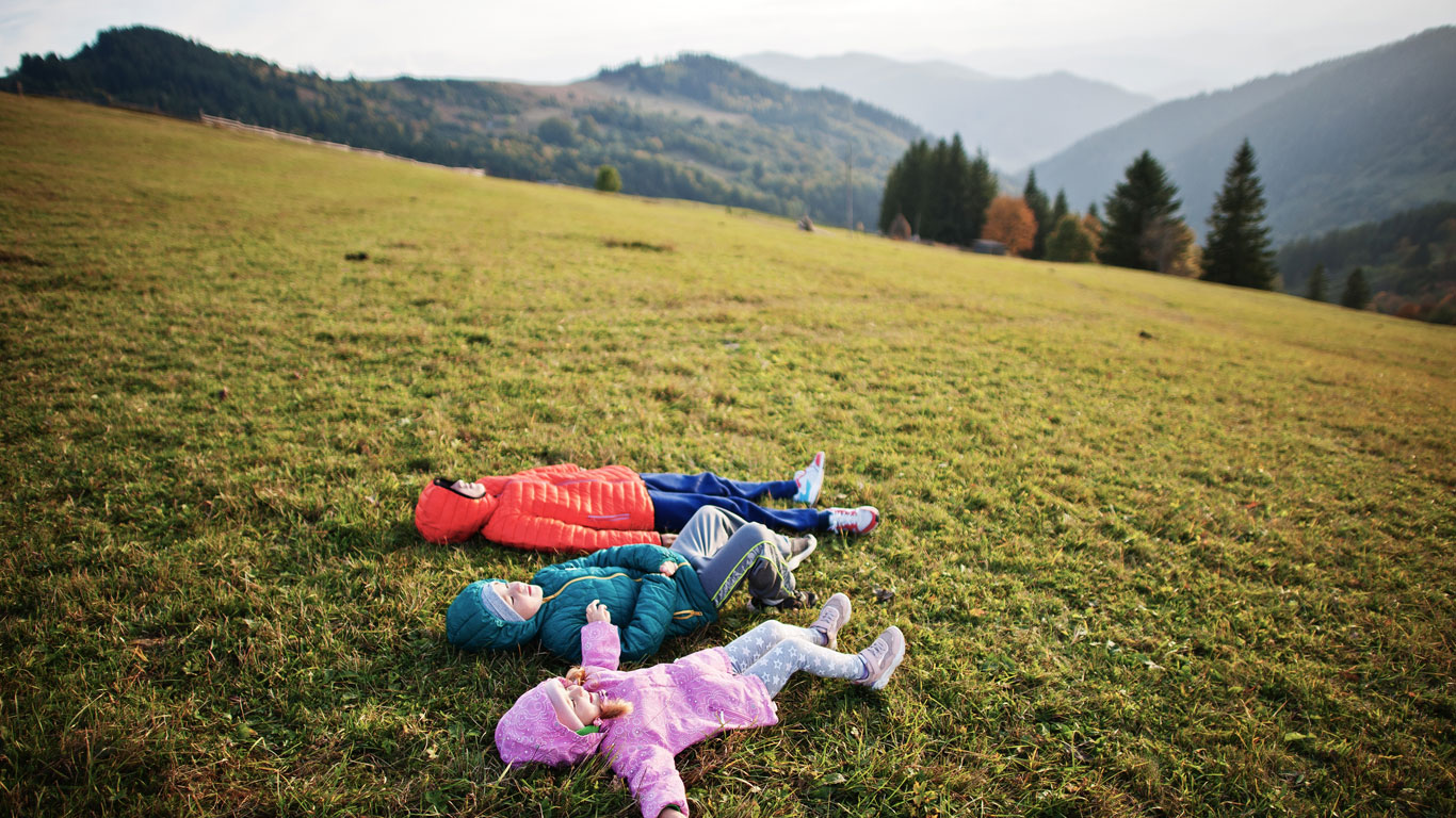 Tre bambini sdraiati sul prato in montagna
