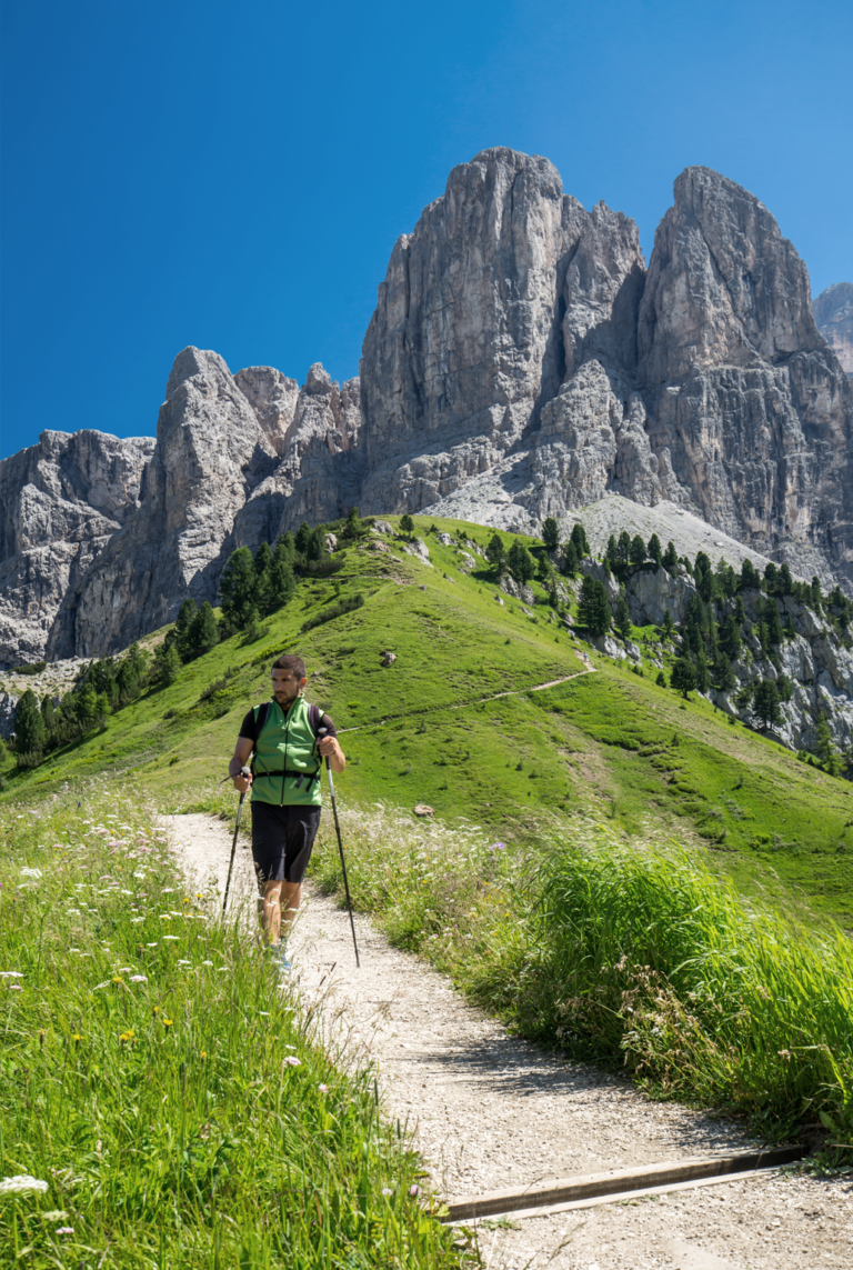 Uomo che sta facendo nordic walking in un sentiero con alle spalle le dolomiti venete